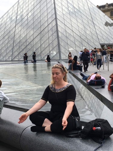 Kvinde mediterer i yogastilling ved Louvre – som en del af yoga.